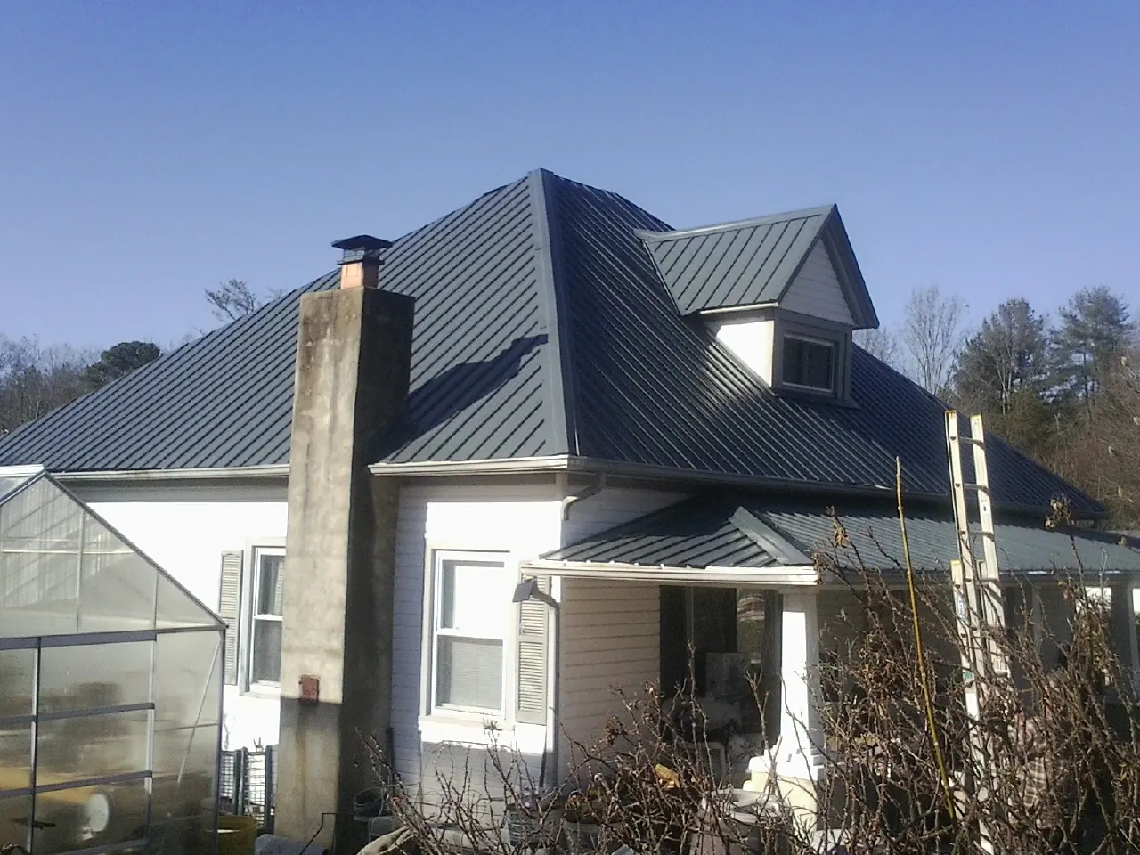 Dark blue standing seam metal roof on a white farmhouse with dormer — Slate & Tile Roof Repair by Roofing Brothers in Glide
