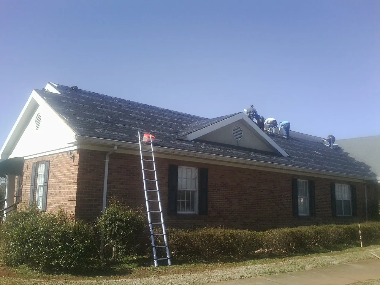 Crew tearing shingles off a brick ranch roof with a ladder set — Emergency Roof Repair work by our crew in Glide