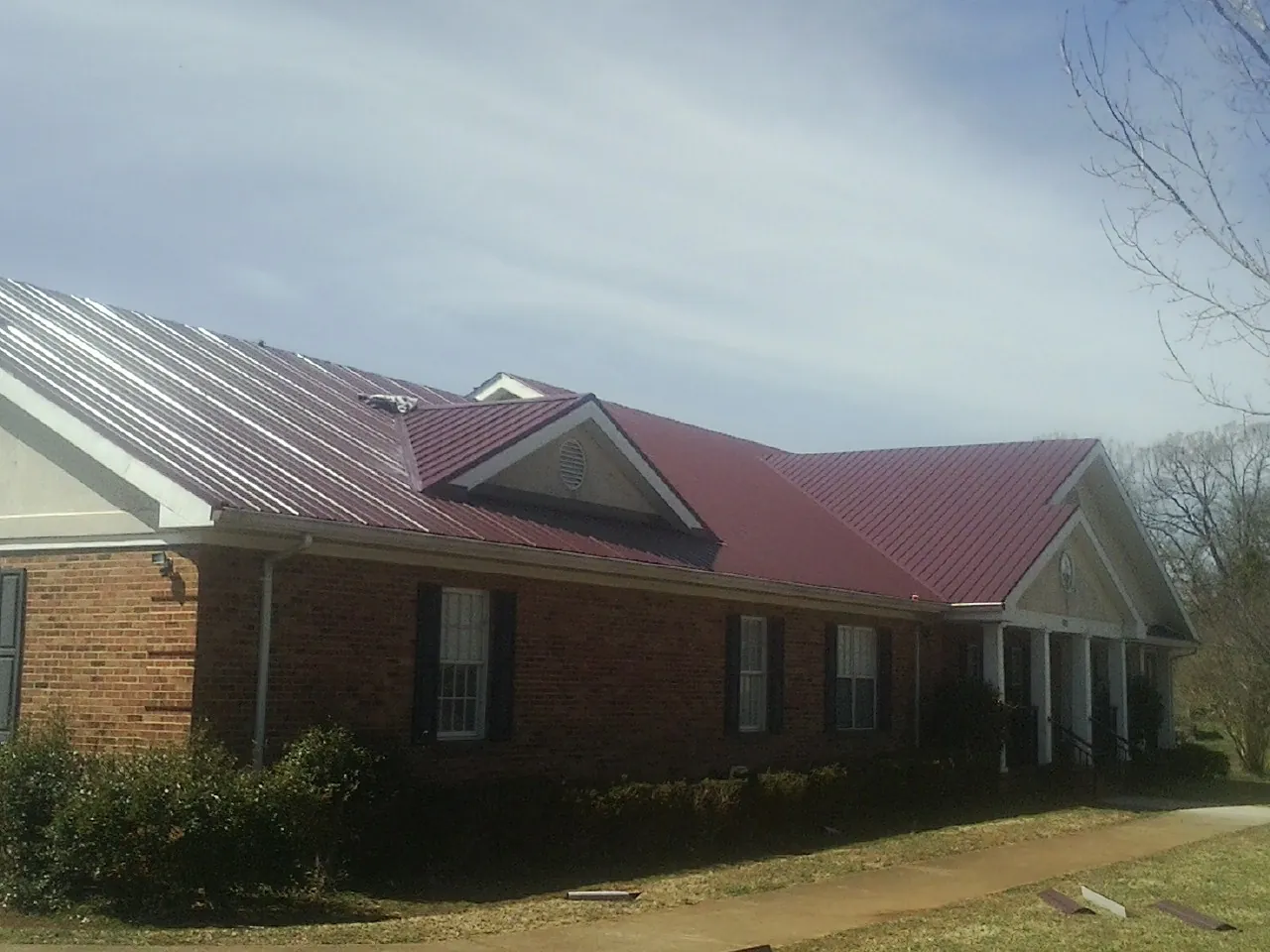 Red metal roof with gabled entries on a long brick building, from a Hail Damage Roof Repair job in Glide