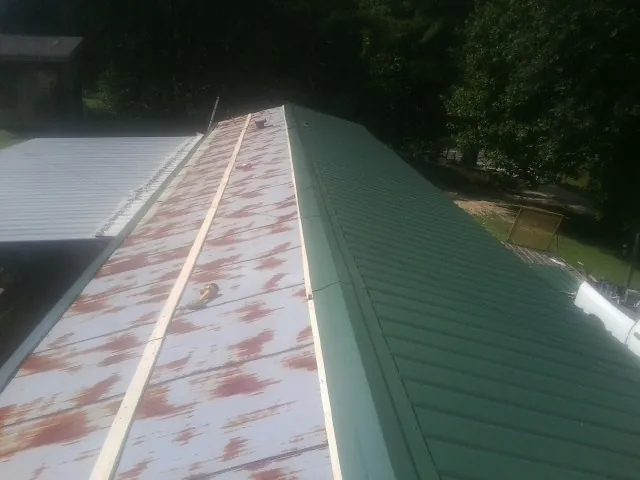 Old rusted panels beside newly installed green metal roofing — Wind Damage Roof Repair by Roofing Brothers in Glide