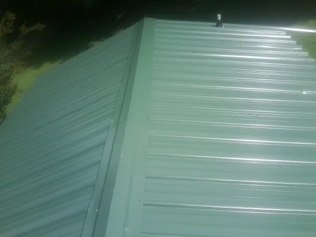 New green metal panels meeting at the ridge of a roof — Flat Roof Repair work by our crew in Glide