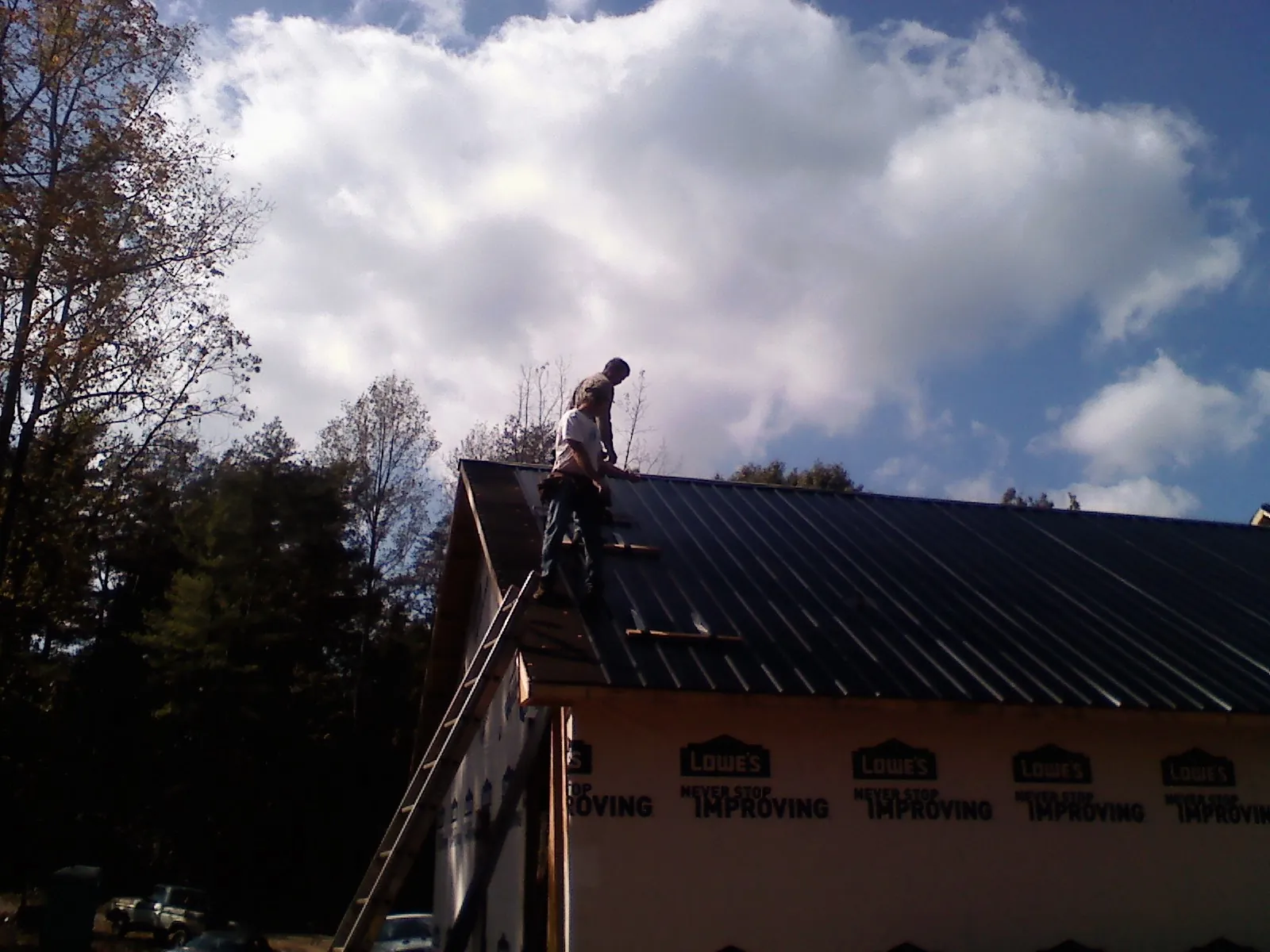 Roofer fastening dark metal panels high against a cloudy sky, from a Roof Inspection job in Glide