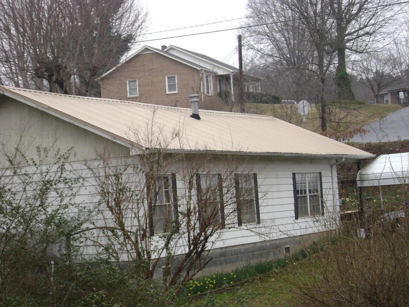 Tan metal roof on a white sided house set into a hillside — Commercial Roofing by Roofing Brothers in Glide